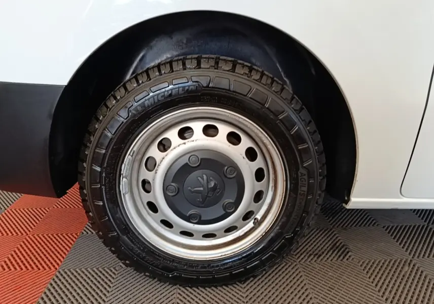 Gros plan sur la roue arrière droite d’un Peugeot Expert Fourgon blanc, jante acier avec logo Peugeot central.