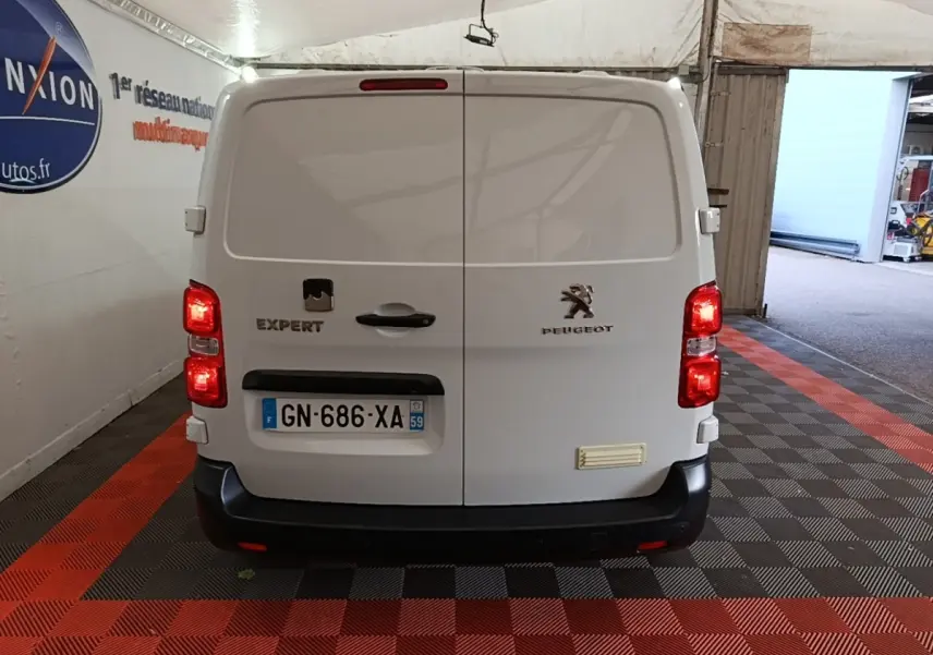 Vue arrière d’un Peugeot Expert Fourgon blanc garé dans un garage avec feux arrière allumés.
