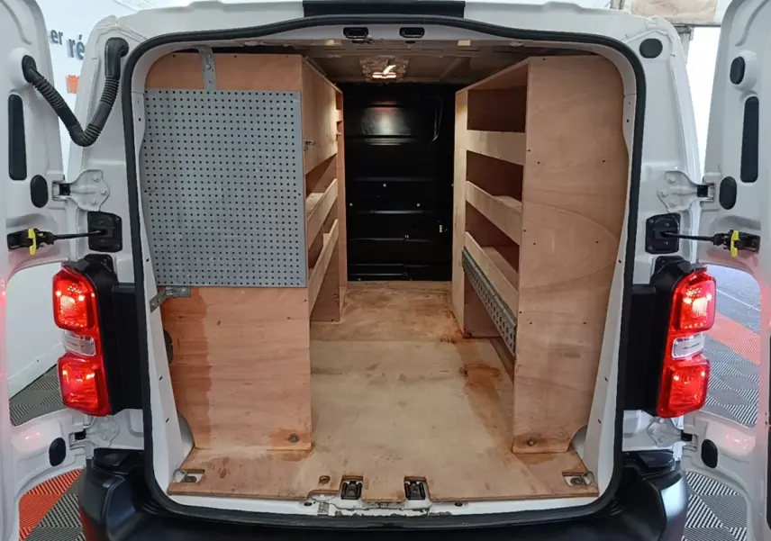 Vue arrière du Peugeot Expert Fourgon blanc 2023 avec portes ouvertes, montrant l’aménagement intérieur en bois pour rangement.
