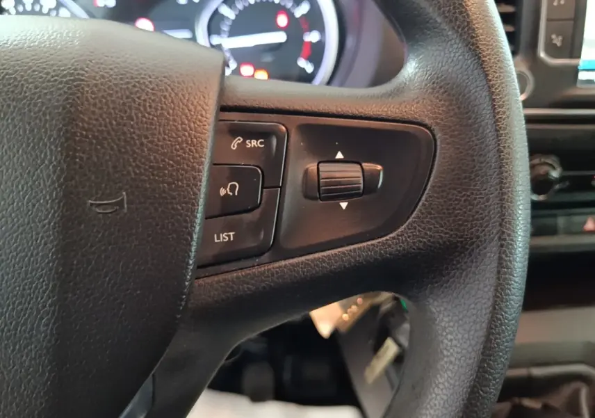 Gros plan sur le volant noir du Peugeot Expert Fourgon avec commandes audio et tableau de bord lumineux en arrière-plan.