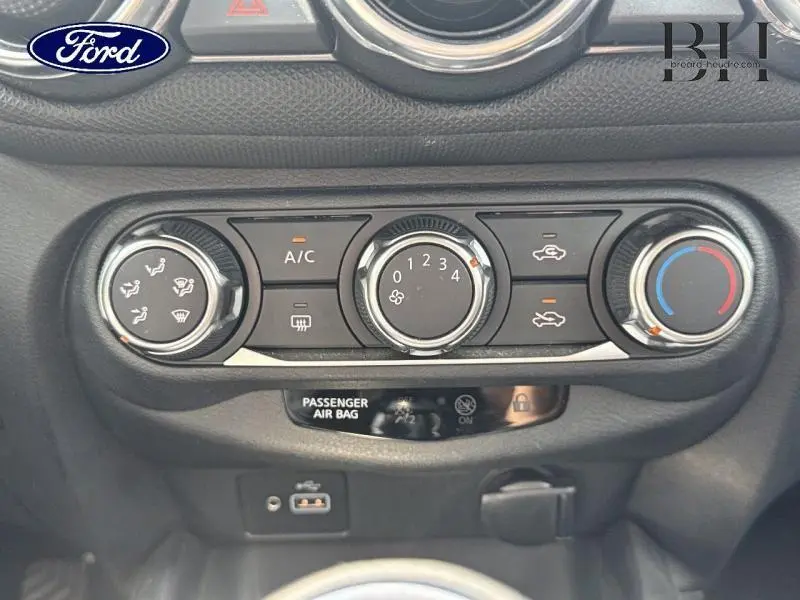 Tableau de bord avec commandes de climatisation manuelle et voyants airbag d'une Nissan Juke gris perle métallisé.