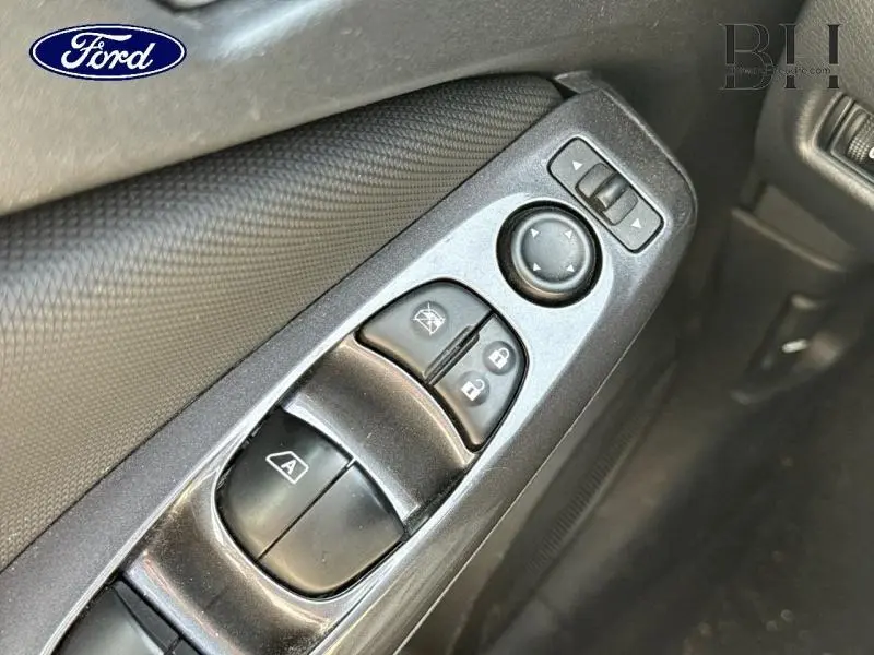 Gros plan sur les commandes de vitres et rétroviseurs côté conducteur d'une portière intérieure noire.