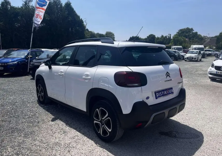 Vue 3/4 arrière droite d'un Citroën C3 Aircross blanc Banquise avec toit blanc et barres de toit noires.