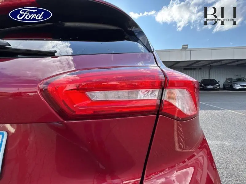 Gros plan sur le feu arrière droit d'une Ford Focus 1.0 EcoBoost 125ch rouge Premium Candy sous un ciel partiellement nuageux.