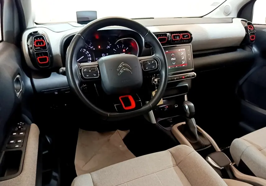 Intérieur de Citroën C3 Aircross 2020, vue du poste de conduite avec volant cuir noir et touches rouges sur aérateurs.