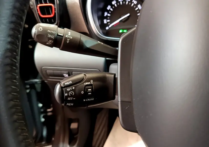 Gros plan sur les commandes au volant cuir du Citroën C3 Aircross gris foncé, avec tableau de bord partiellement visible.