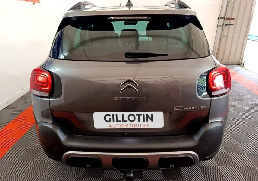 Vue arrière d'un Citroën C3 Aircross gris foncé avec feux arrière allumés et barres de toit visibles.