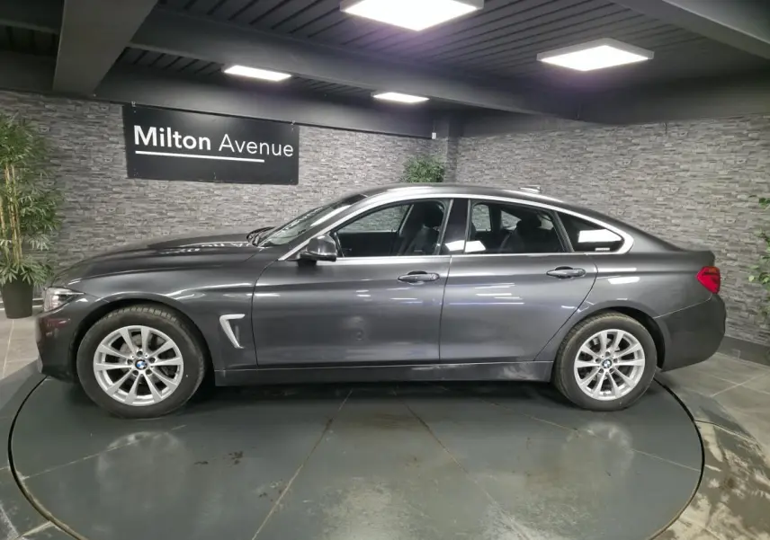 BMW Série 4 Gran Coupé gris foncé vue de profil côté gauche avec jantes alliage 17 pouces en intérieur showroom.