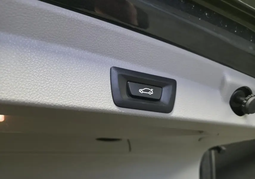 Bouton d'ouverture électrique du hayon sur la face intérieure du coffre d'une BMW Série 4 gris foncé.
