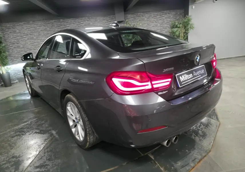 BMW Série 4 Gran Coupé gris foncé vue 3/4 arrière droit avec feux LED et double sortie d’échappement ronde à gauche.