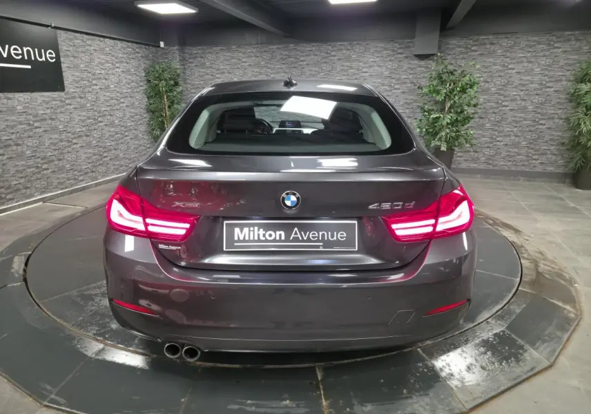 Vue arrière d'une BMW Série 4 420d xDrive Gran Coupé gris foncé avec feux LED allumés en intérieur showroom.