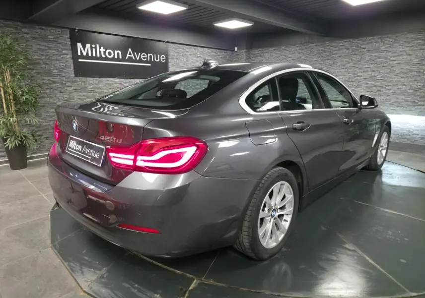 BMW Série 4 420d xDrive Gran Coupé gris foncé vue 3/4 arrière droit avec feux arrière LED allumés.