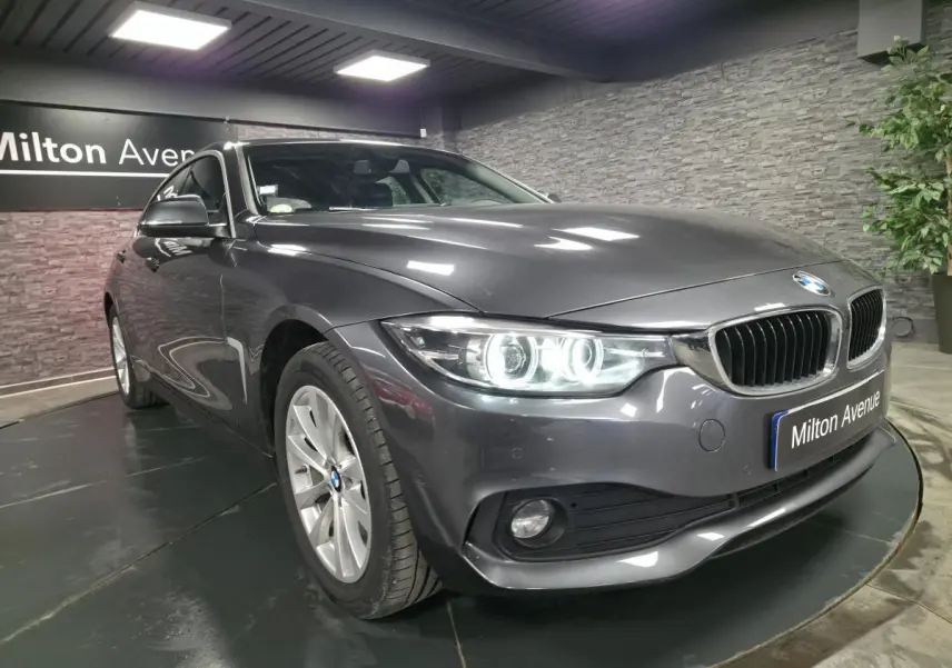 BMW Série 4 Gran Coupé gris foncé vue 3/4 avant avec phares LED allumés et calandre chromée.