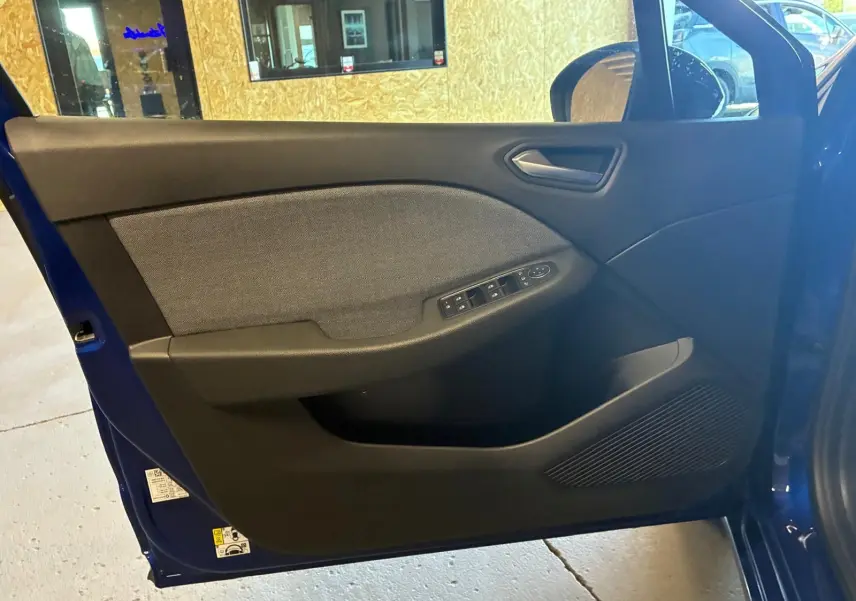Vue intérieure de la porte avant gauche d'une Renault Clio Bleu Iron 2025, avec commandes de vitres et tissu gris.