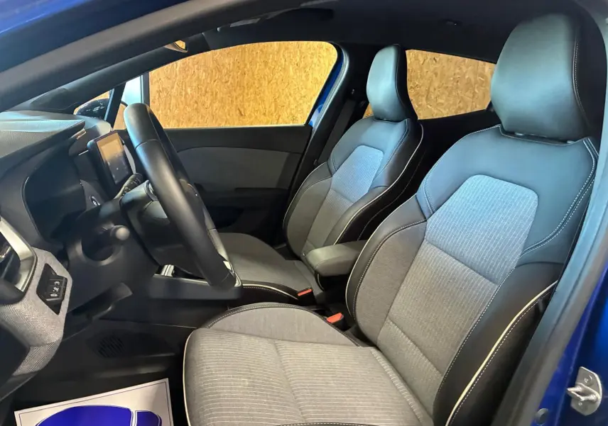 Vue intérieure côté conducteur de la Renault Clio V E-TECH 145 TECHNO 2025, sièges tissu gris noir et volant visible.