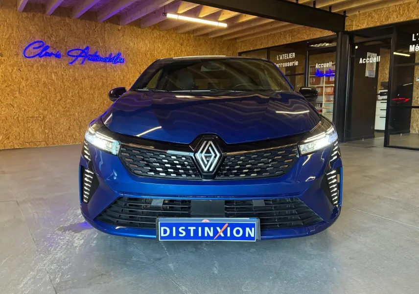 Vue de face d'une Renault Clio V E-TECH 145 TECHNO bleu iron avec calandre noire et phares LED allumés.