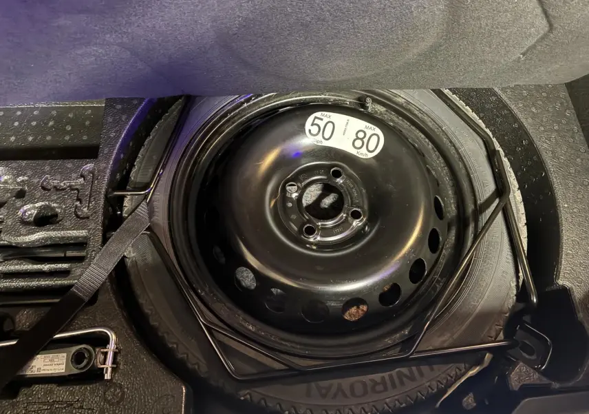 Gros plan sur la roue de secours noire dans le coffre d’une Renault Clio V E-TECH 145 Bleu Iron, avec outils de changement visibles.