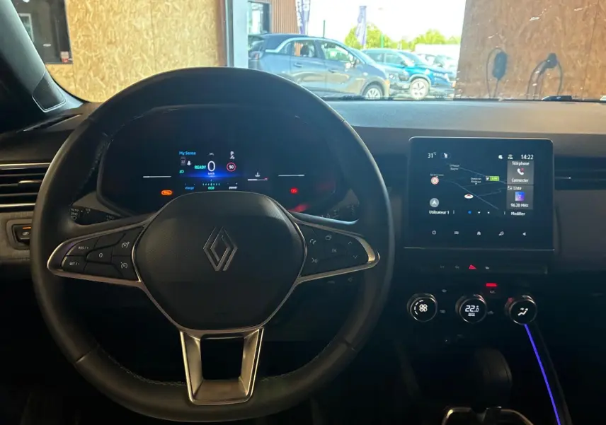 Vue intérieure centrée sur le volant Renault Clio V E-TECH 145 bleu Iron, avec tableau de bord numérique et écran tactile.
