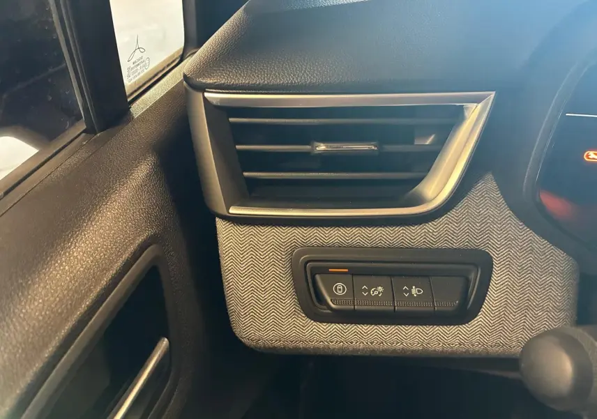 Détail intérieur côté gauche montrant la grille d'aération et les commandes d'éclairage sur tissu gris noir de la Renault Clio 2025.