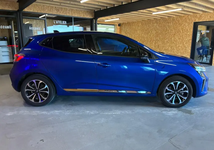 Profil droit d'une Renault Clio V E-TECH 145 TECHNO bleu iron 2025 avec jantes alliage bicolores et vitres teintées.