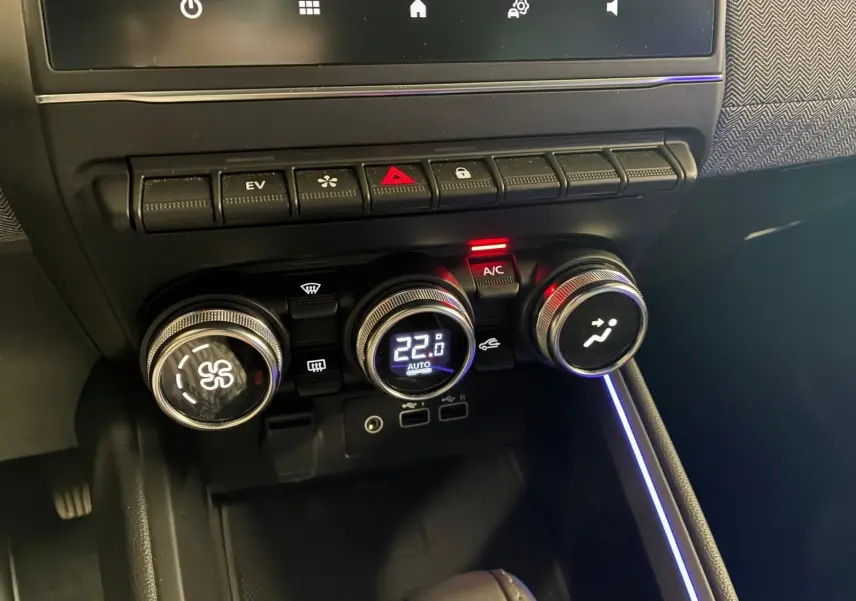 Gros plan sur la console centrale de la Renault Clio V E-TECH 145 TECHNO, avec commandes de climatisation et éclairage d'ambiance bleu.
