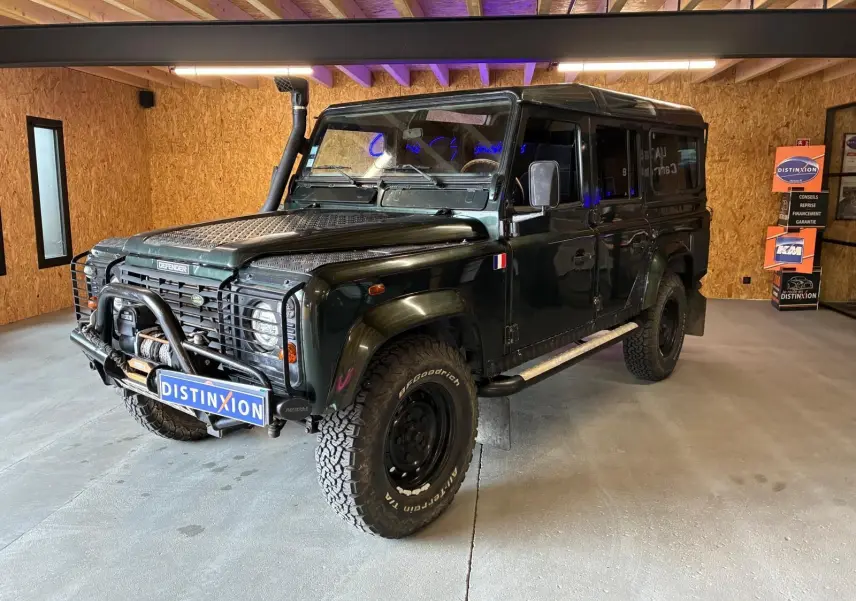 Land Rover Defender 110 vert vue 3/4 avant droit avec treuil, plaques de protection et pneus tout-terrain.