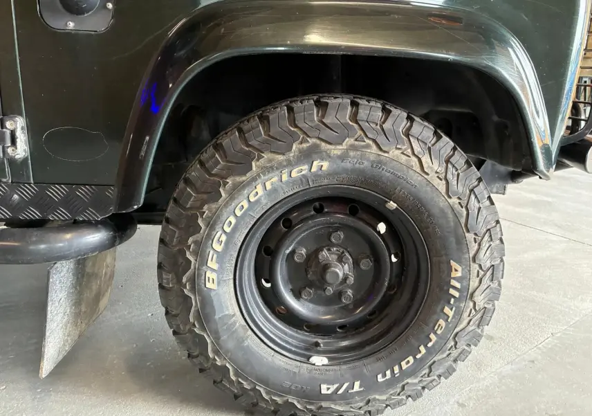 Gros plan sur la roue avant gauche du Land Rover Defender 110 vert 2005 avec pneu BFGoodrich tout-terrain.