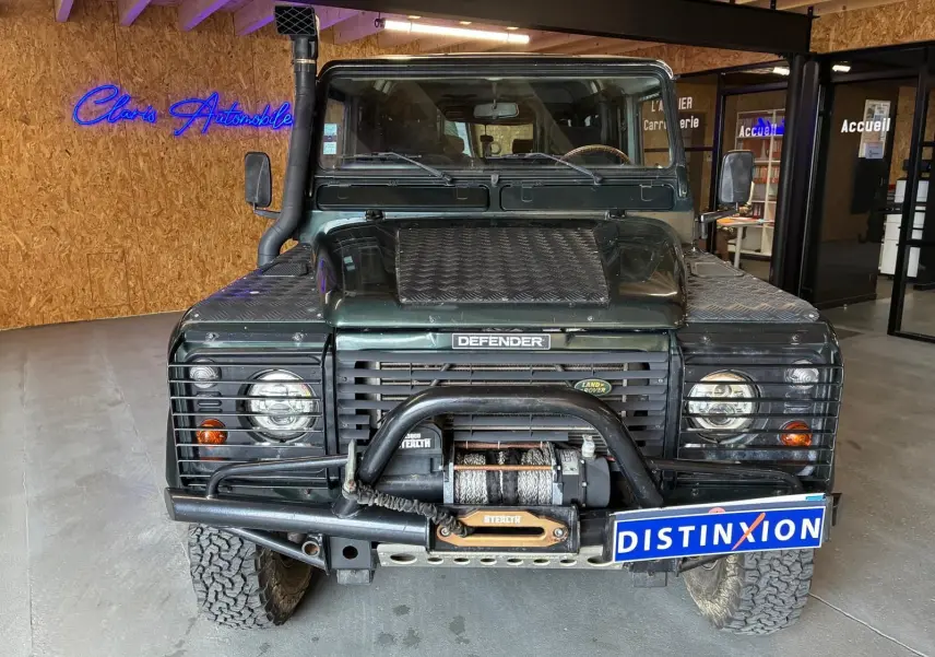 Vue frontale d’un Land Rover Defender 110 vert foncé de 2005 avec treuil et protections sur les phares.