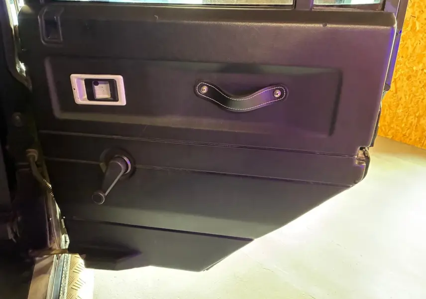 Vue rapprochée de la porte intérieure côté gauche du Land Rover Defender 110 2005, avec poignée et manivelle de vitre.