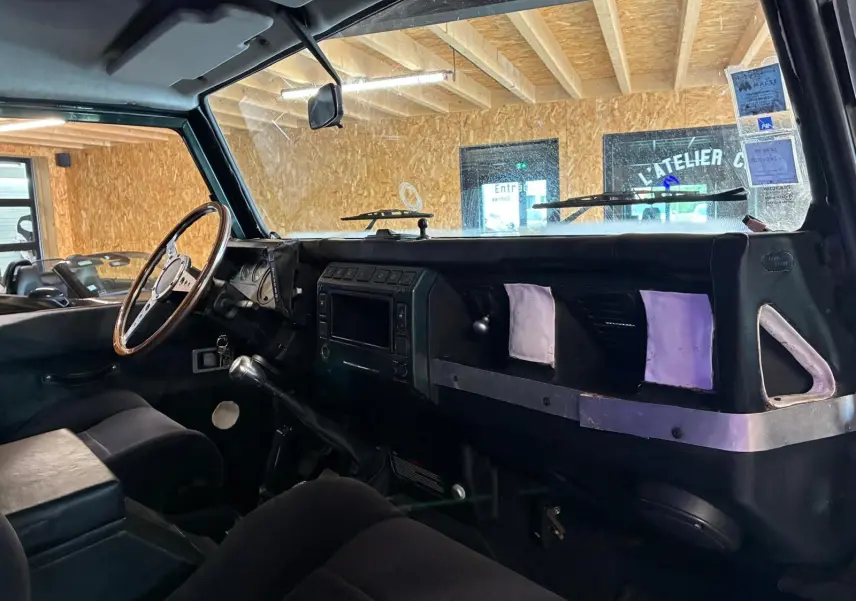 Vue intérieure côté conducteur du Land Rover Defender 110 2005, tableau de bord noir avec volant bois et levier de vitesse manuel.