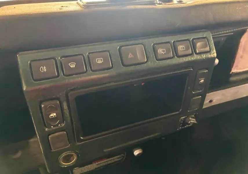 Détail du tableau de bord vert foncé du Land Rover Defender 110 2005, montrant les boutons de commande et la console centrale.