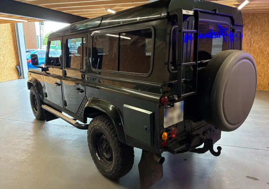 Land Rover Defender 110 vert vue 3/4 arrière droit, avec roue de secours et échelle sur porte arrière.