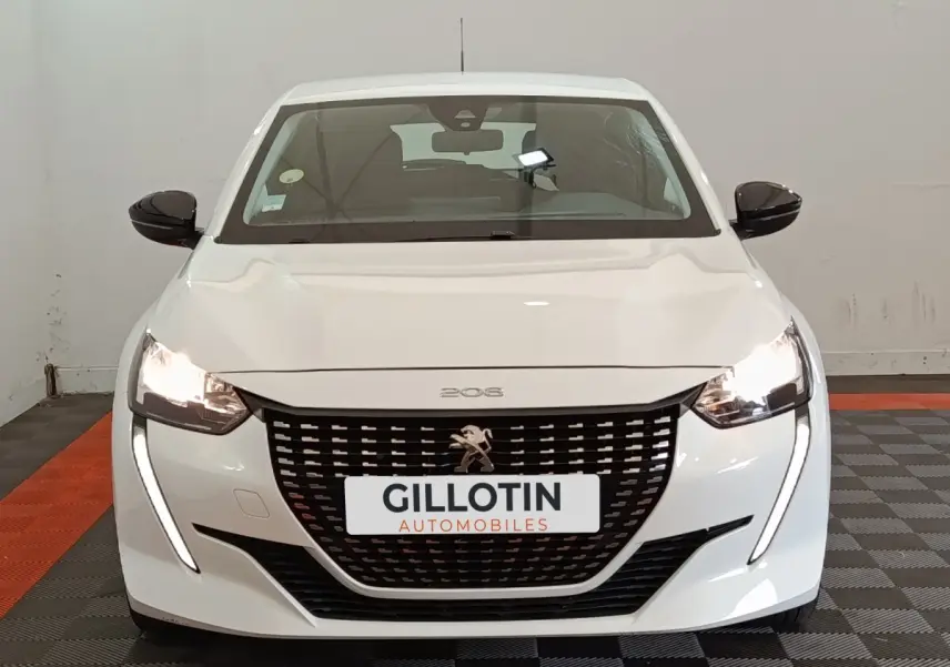 Vue avant d'une Peugeot 208 blanche avec feux allumés et calandre noire distinctive dans un showroom.
