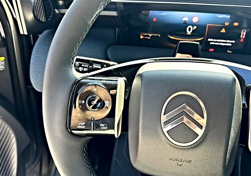 Gros plan sur le volant multifonction noir du Citroën C5 Aircross 2026 avec logo chromé et tableau de bord numérique en arrière-plan.