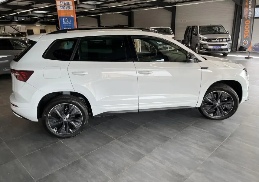 Profil droit du SUV blanc SKODA KAROQ 2025 version Sportline avec jantes alliage noires et détails noirs brillants.