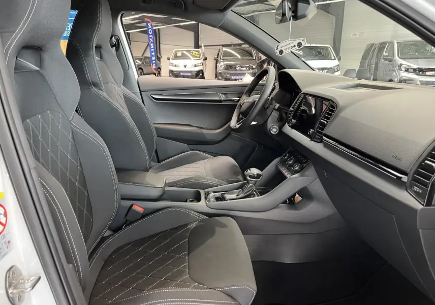 Intérieur du SKODA KAROQ 1.5 TSI blanc, vue côté conducteur, sièges sport noirs avec surpiqûres blanches et tableau de bord moderne.