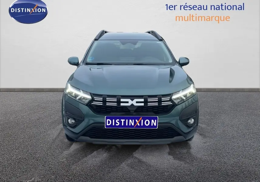 Vue avant d'une Dacia Jogger 2025 vert cèdre métal avec calandre noire et phares LED allumés.