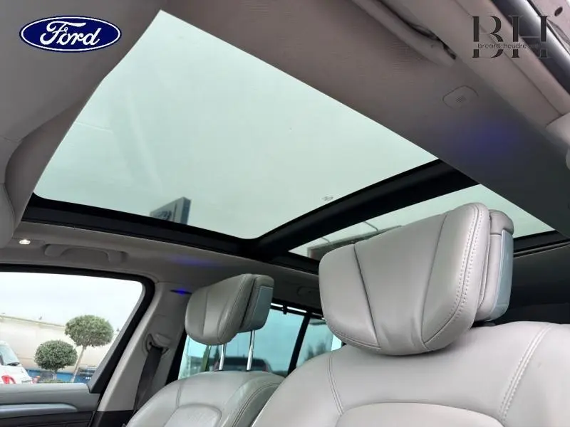 Vue intérieure sur les sièges avant en cuir clair et le toit panoramique vitré d'un Renault Espace blanc Glacier.