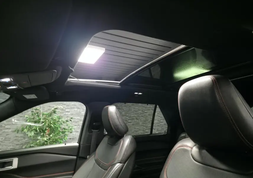 Vue intérieure du Ford Explorer gris, montrant les sièges avant en cuir noir avec surpiqûres rouges et toit panoramique ouvert.