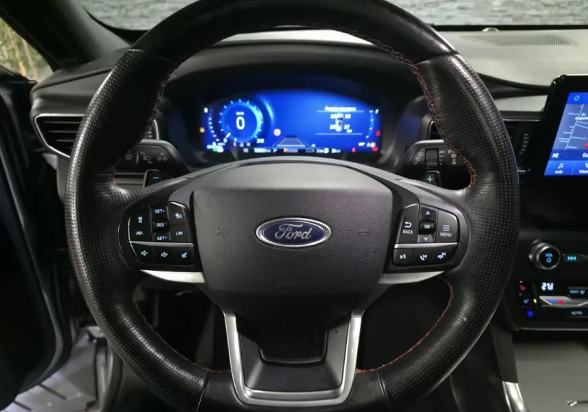 Vue rapprochée du volant noir perforé avec surpiqûres rouges du Ford Explorer 2020, tableau de bord numérique bleu en arrière-plan.