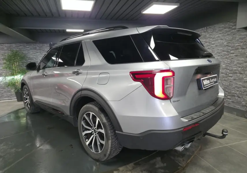 Vue 3/4 arrière droit du Ford Explorer gris métallisé avec attelage et jantes alliage noires brillantes en intérieur showroom.
