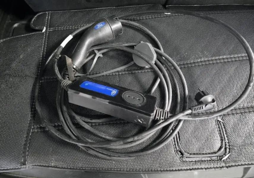Câble de recharge noir Ford posé sur un tapis de coffre noir, accessoire du Ford Explorer hybride rechargeable gris.