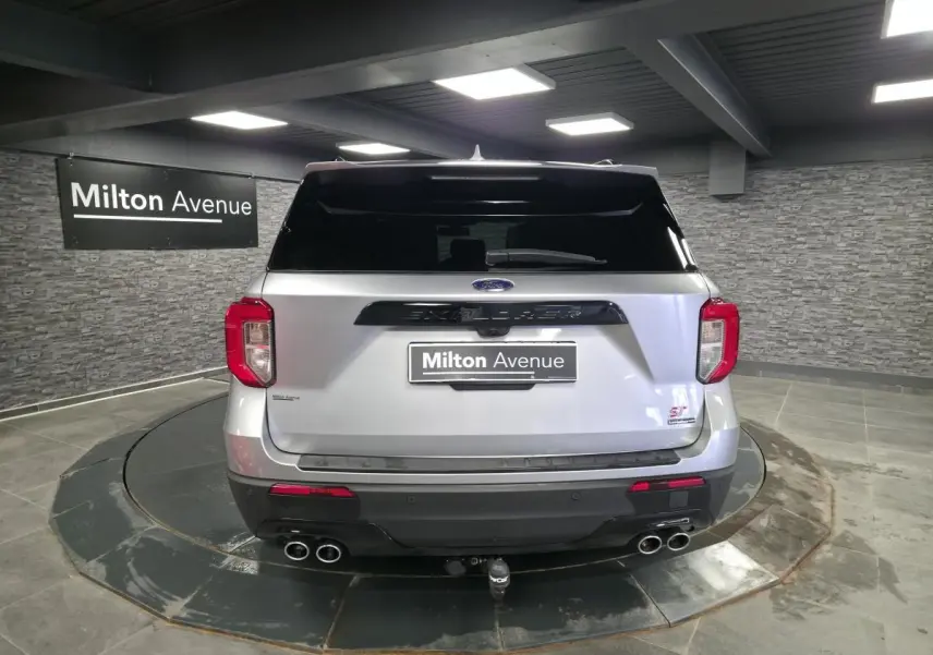 Vue arrière d'un Ford Explorer gris métallisé avec quatre sorties d'échappement chromées et attelage visible en intérieur showroom.