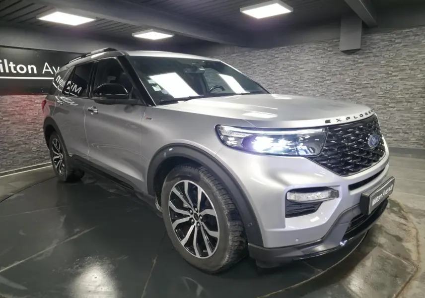 Ford Explorer gris métallisé en vue 3/4 avant droit, avec calandre noire brillante et jantes alliage 20 pouces.