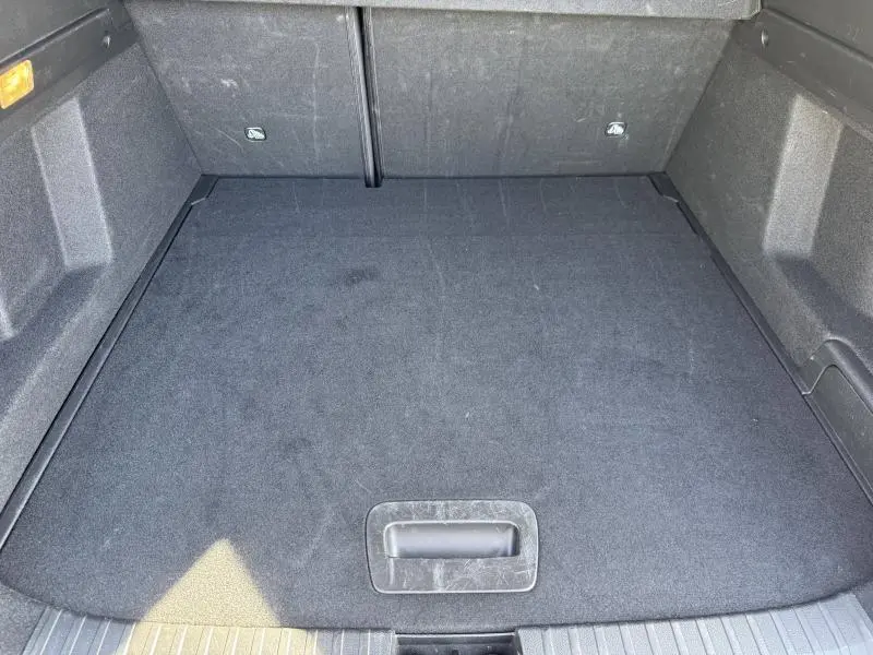 Vue du coffre spacieux et propre de la Renault Arkana 1.6 E-Tech noir métal, avec tapis noir et éclairage latéral.