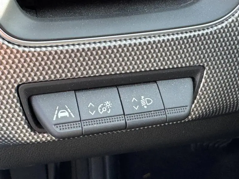 Gros plan sur les commandes d’aide à la conduite et réglage des phares du tableau de bord du Renault Arkana noir métal.