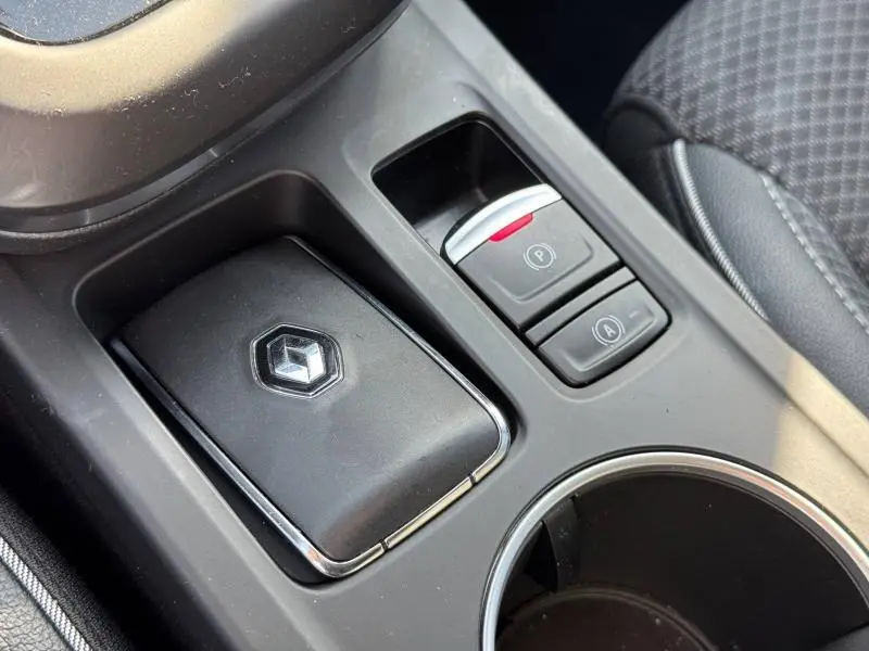 Gros plan sur la console centrale noire du Renault Arkana 2023, avec bouton de frein à main électronique et porte-clés.