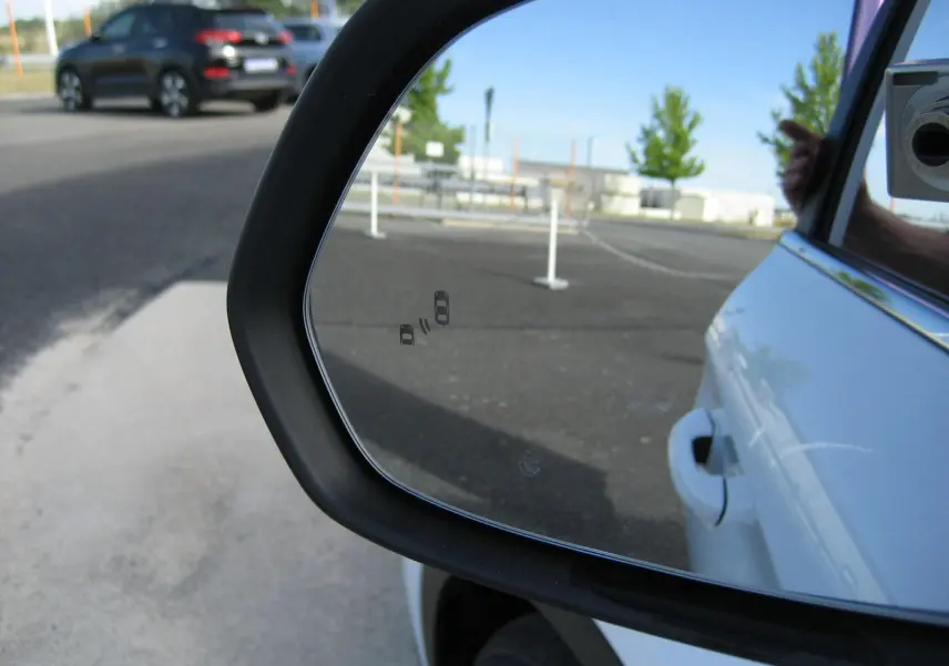 Rétroviseur côté droit du MG ZS blanc 2026, avec reflet du véhicule et vue partielle d’une voiture noire à l’arrière.