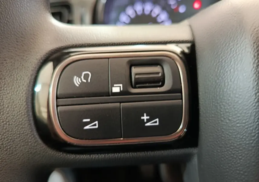Gros plan sur les commandes multifonctions noires du volant de la Citroën C3 blanche, avec boutons de volume et gestion d'appels.