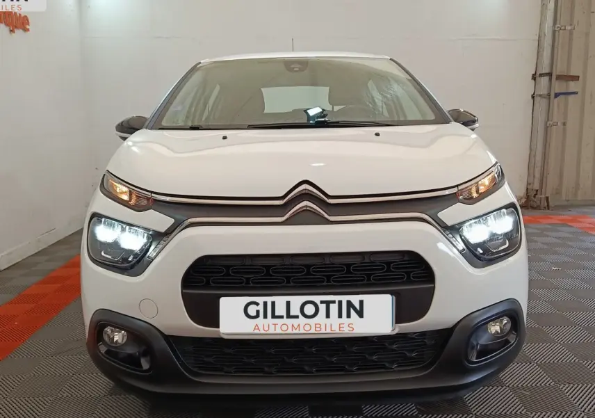 Vue frontale d'une Citroën C3 blanche 2022 avec phares LED allumés dans un garage.